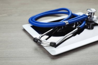 Tahta masada steteskoplu bilgisayar tableti, yakın plan. Metin için boşluk