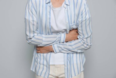 Açık gri arka planda adet sancısı çeken genç bir kadın, yakın plan.