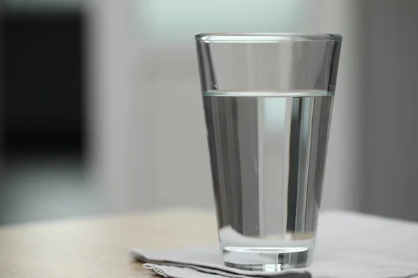 Glass of pure water on table against blurred background, space for text