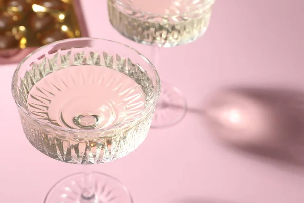 Glasses of expensive white wine on pink background, closeup. Space for text