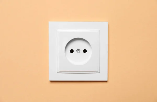 Power socket on pale orange wall. Electrical supply