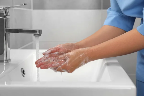 Doctor washing hands with water from tap in bathroom, closeup
