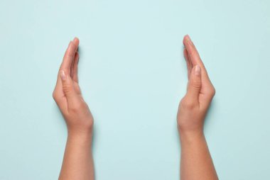 Açık mavi arka planda tutulan bir kadın, ellerin yakın çekimi. Metin için boşluk