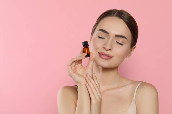 Young woman with bottle of essential oil on pink background, space for text