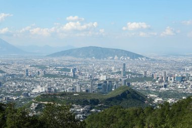 Güzel gökyüzü altında ağaçlar, dağlar ve binalar olan şehir manzarası.