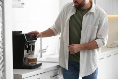 Genç adam mutfakta modern makineyle taze aromatik kahve hazırlıyor.