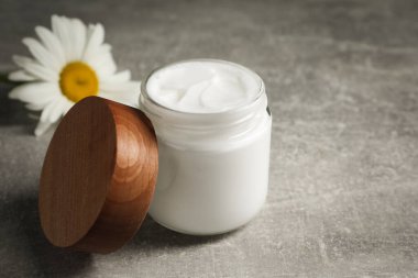 Yüz kremi kavanozu ve gri masada güzel papatya çayı. Metin için boşluk