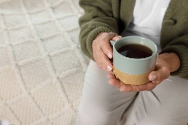 Kapalı mekanda bir fincan sıcak içecekle yaşlı bir kadın, yakın plan. Ev bakımı hizmeti