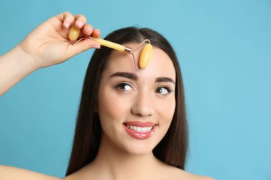 Açık mavi arka planda doğal yeşil yüz silindiri kullanan kadın