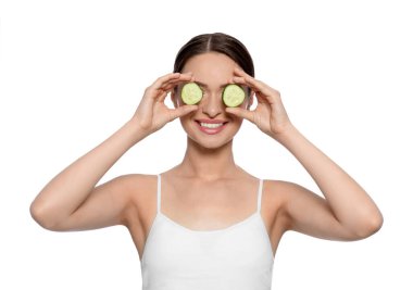 Beyaz arka planda salatalık dilimleri olan genç bir kadın. Göz bakımı