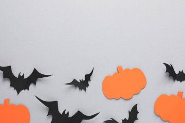 Açık gri zemin üzerinde kağıt yarasalar ve balkabaklarıyla düz kompozisyon, metin için boşluk. Cadılar Bayramı Dekorasyonu