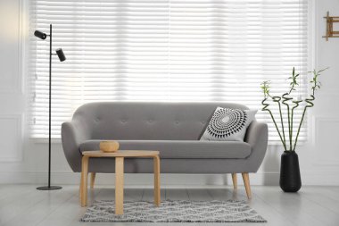 Vase with green bamboo stems near sofa in living room interior