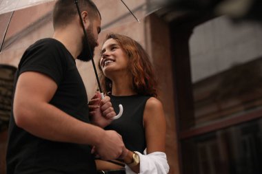 Şemsiyeli genç çift yağmur altında birlikte vakit geçiriyorlar. Şehir caddesinde, mesaj için yer var.