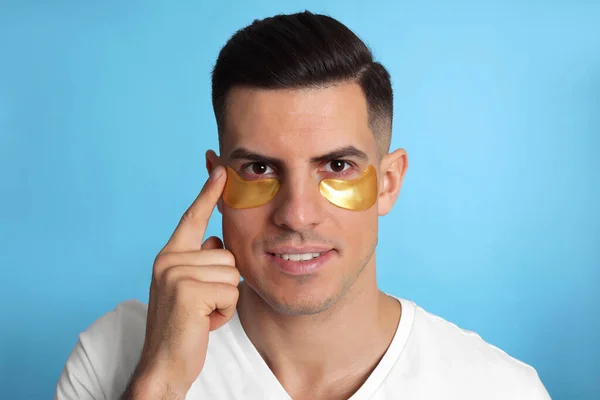 Man Applying Golden Eye Patch Light Blue Background — Stock Photo, Image