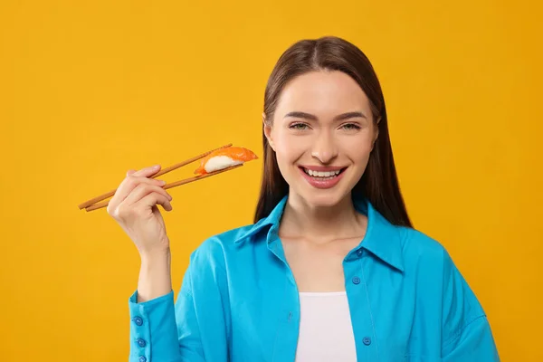 オレンジを背景に箸で寿司を握る幸せな若い女性 — ストック写真