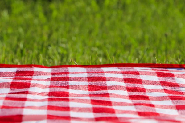 Checkered picnic tablecloth on fresh green grass, closeup