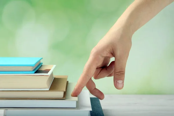 Woman climbing up stairs of books with fingers on white wooden table against blurred background, closeup