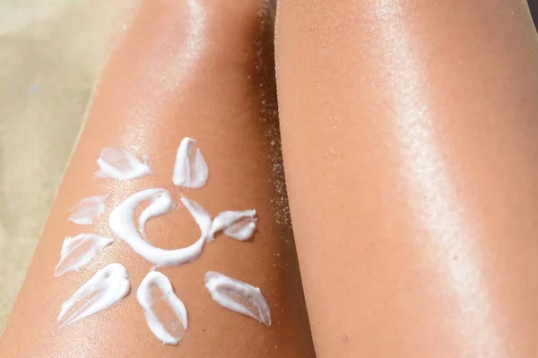 Sun drawn with sunscreen on woman\'s leg at beach, closeup
