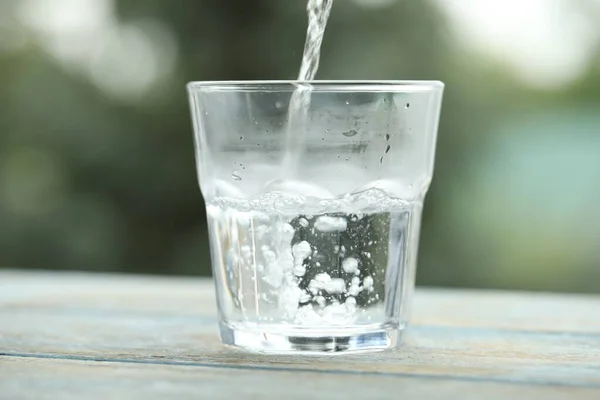 Pouring pure water into glass on light blue wooden table against blurred background