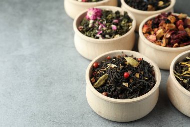 Açık gri masadaki ahşap kaselerde farklı türde kuru bitkisel çay. Metin için boşluk