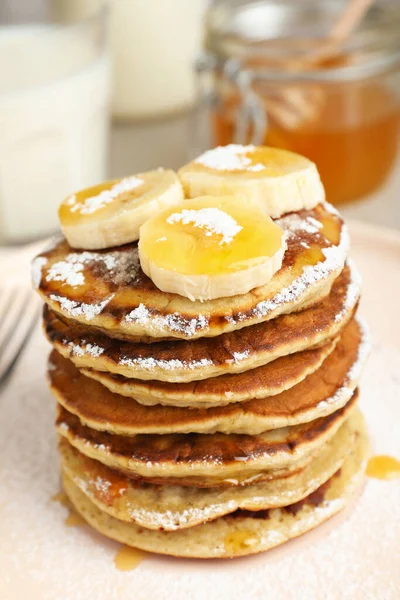 Banana pancakes with honey and powdered sugar on plate, closeup