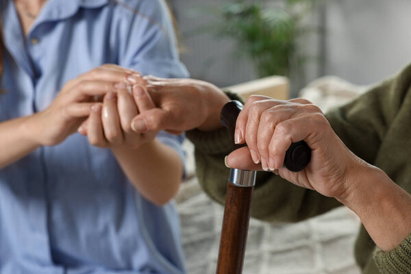 Caregiver and elderly woman with walking cane at home, closeup