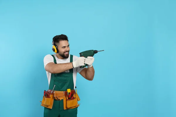 Young worker in uniform with power drill on light blue background. Space for text