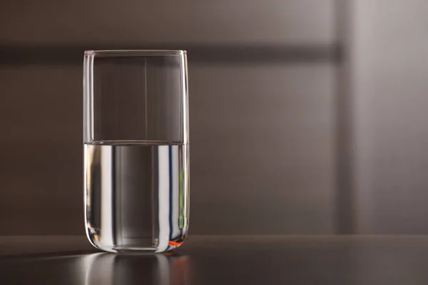 Glass of pure water on table against blurred background, space for text