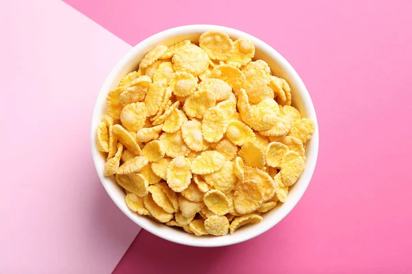 Bowl of tasty crispy corn flakes on pink background, top view