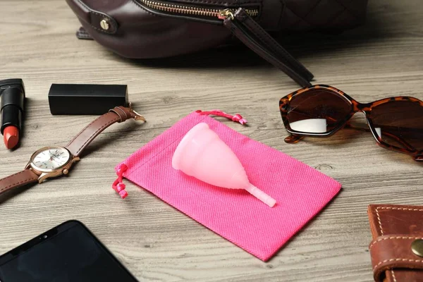 Menstrual cup and different women\'s accessories on wooden table
