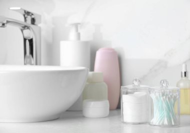 Containers with cotton swabs and pads near cosmetic products on white countertop in bathroom