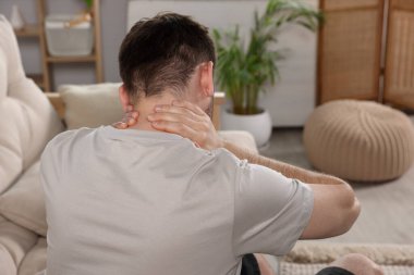 Man suffering from neck pain in living room, back view
