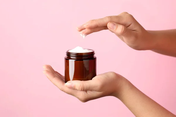 Woman with jar of face cream on pale pink background, closeup