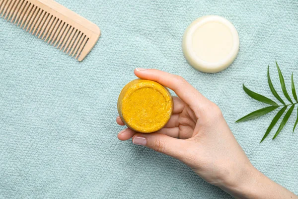 Woman holding solid shampoo bar near light blue tablecloth, top view. Hair care