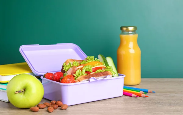 健康食品と緑の黒板の近くの木製のテーブルの上に異なる文房具と弁当箱 — ストック写真