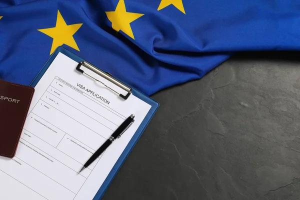 Visa application form, passport, pen and flag of European Union on black table, flat lay. Space for text