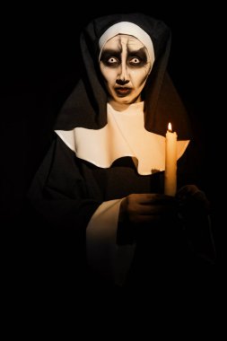 Siyah arka planda yanan mumu olan korkunç şeytani bir rahibe. Cadılar Bayramı partisi görünüşü