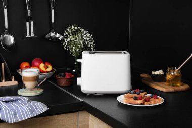 Modern tost makinesi, taze böğürtlenli ekmek ve mutfak tezgahında kahve.