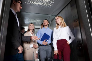 Bir grup ofis çalışanı modern asansörde konuşuyor.