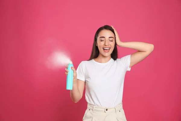 Young woman applying dry shampoo against pink background