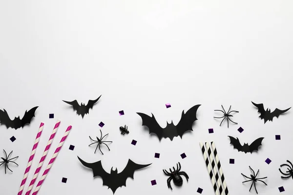 Flat lay composition with paper bats, spiders and straws on white background, space for text. Halloween celebration