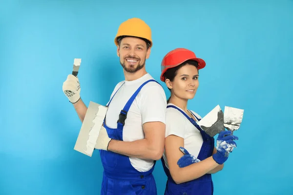 Professional workers with putty knives in hard hats on light blue background