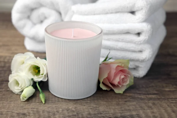 Scented candle, folded towels and flowers on wooden table