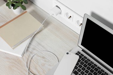Laptop ve akıllı telefon ahşap masada şarj oluyor.