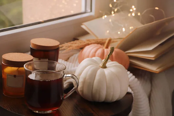 Cup of hot drink, candles and pumpkins on window sill indoors
