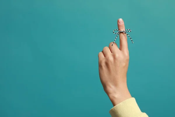 Woman showing index finger with tied bow as reminder on light blue background, closeup. Space for text