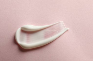 Pembe arka planda yüz kremi örneği, üst görünümde.