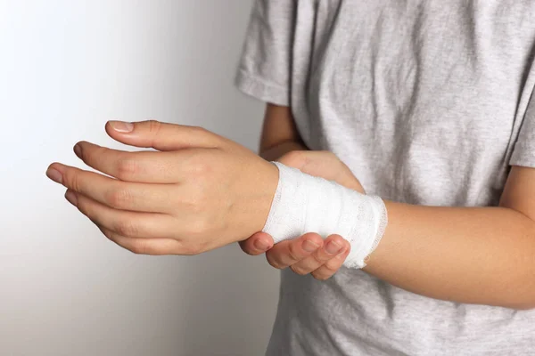 Woman with wrist wrapped in medical bandage on light grey background, closeup