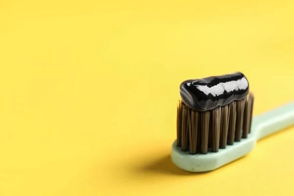 Brush with charcoal toothpaste on yellow background, closeup. Space for text