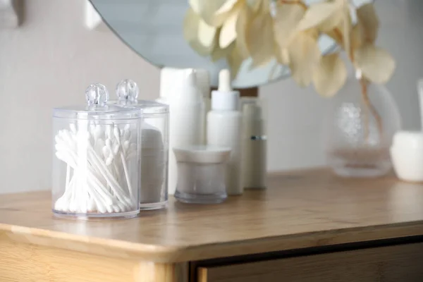 Containers with cotton swabs and pads near cosmetic products on dressing table